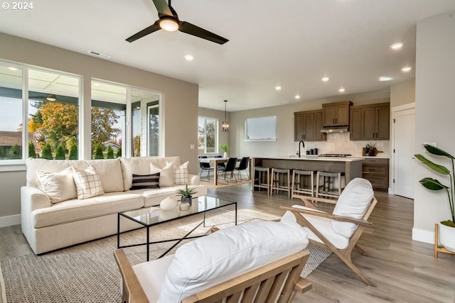 living room with ceiling fan with notable chandelier, light wood-type flooring, and sink