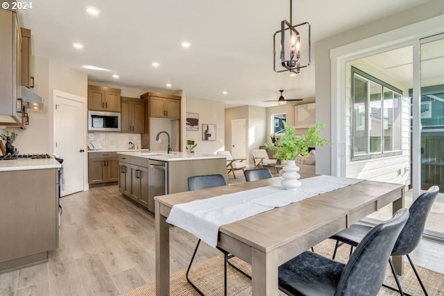 dining space with ceiling fan with notable chandelier, light wood-type flooring, and sink