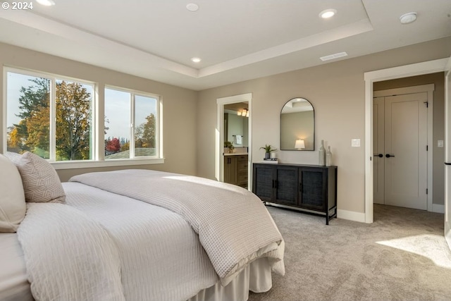 bedroom with a raised ceiling, light colored carpet, and connected bathroom