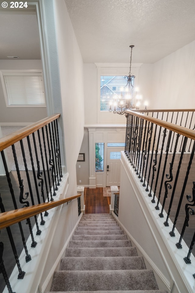 staircase with hardwood / wood-style flooring, a textured ceiling, and an inviting chandelier