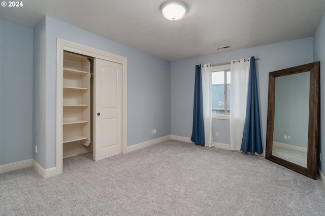 unfurnished bedroom with a closet, a textured ceiling, light colored carpet, and a walk in closet