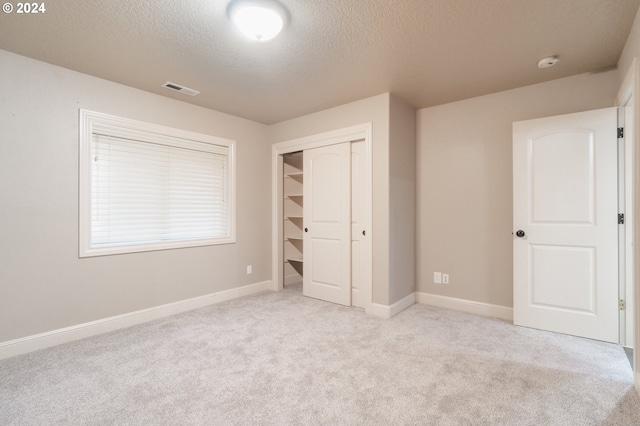 unfurnished bedroom featuring a closet, a textured ceiling, and light colored carpet