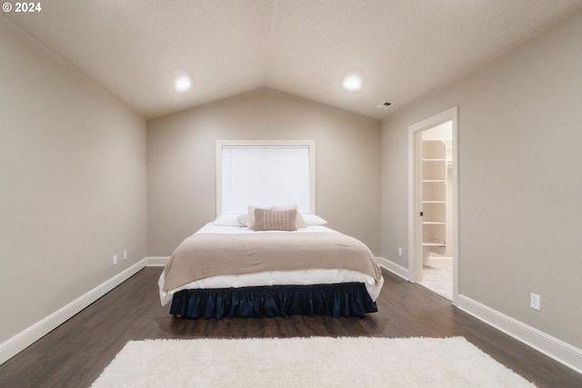 bedroom with a walk in closet, vaulted ceiling, and dark hardwood / wood-style flooring