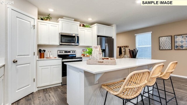 kitchen featuring dark wood-style floors, a breakfast bar, a center island, stainless steel appliances, and white cabinets