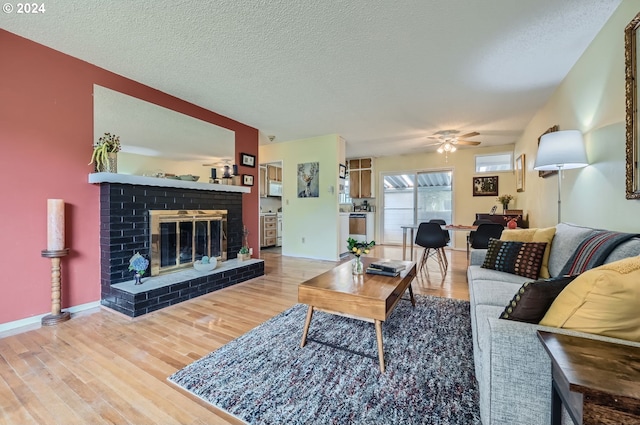 living room with a brick fireplace, a textured ceiling, ceiling fan, and light hardwood / wood-style floors