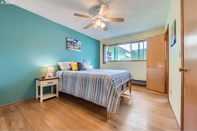 bedroom featuring ceiling fan, a baseboard heating unit, light wood-type flooring, and a textured ceiling