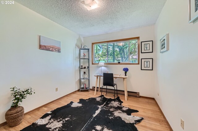 office with light wood-type flooring, baseboard heating, and a textured ceiling