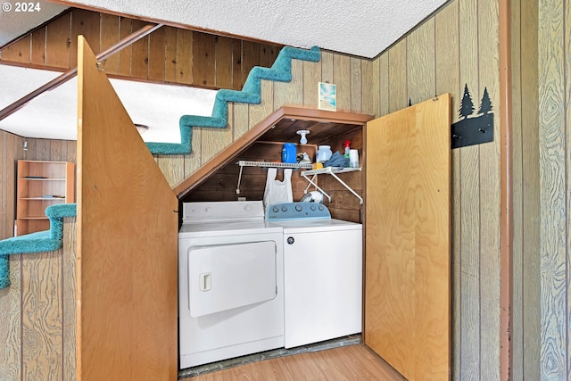 laundry room featuring laundry area, washer and clothes dryer, a textured ceiling, wood walls, and light wood-style floors