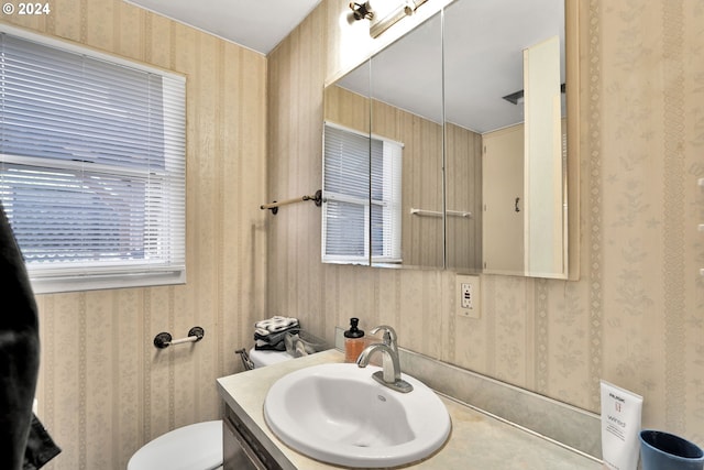 half bath with toilet, vanity, and wallpapered walls