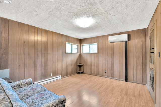 sitting room featuring light wood finished floors, a baseboard heating unit, an AC wall unit, wooden walls, and a textured ceiling