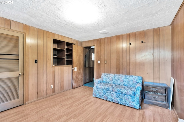 sitting room with wood walls, light wood-style flooring, and a textured ceiling