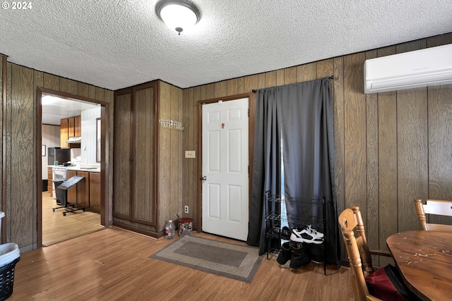 entrance foyer with a textured ceiling, a wall unit AC, and light wood-style flooring