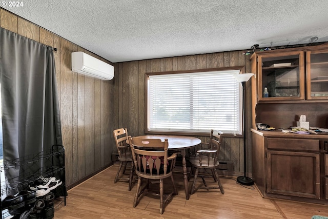 dining room with a textured ceiling, wood walls, a wall unit AC, and light wood-style flooring