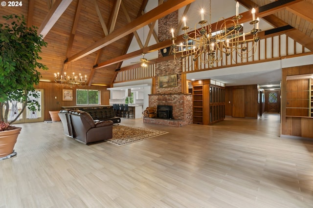 living room with ceiling fan with notable chandelier, a fireplace, light wood-type flooring, high vaulted ceiling, and wooden walls