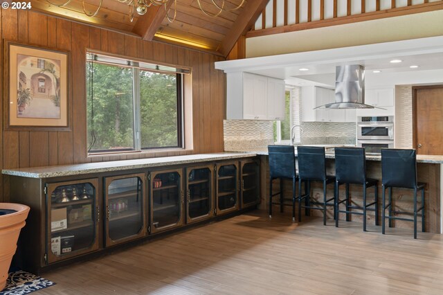 kitchen featuring backsplash, wooden walls, light hardwood / wood-style flooring, wood ceiling, and island range hood