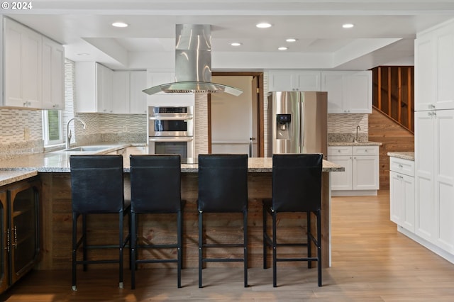 kitchen featuring island exhaust hood, stainless steel appliances, sink, light stone counters, and light wood-type flooring