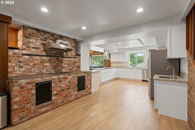 kitchen featuring wall chimney range hood, island exhaust hood, white cabinetry, and light hardwood / wood-style flooring