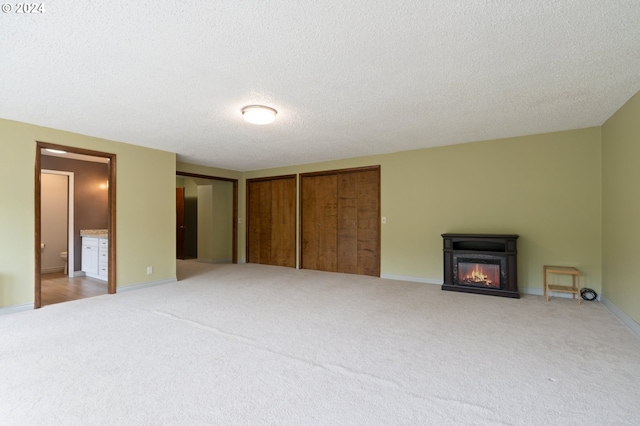 unfurnished bedroom with multiple closets, connected bathroom, light carpet, and a textured ceiling