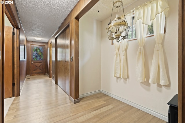 hallway featuring a textured ceiling, light hardwood / wood-style flooring, and wooden walls