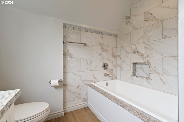 full bathroom featuring toilet, hardwood / wood-style floors, vanity, tiled shower / bath combo, and vaulted ceiling