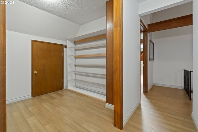 interior space featuring a textured ceiling, lofted ceiling, and light hardwood / wood-style floors