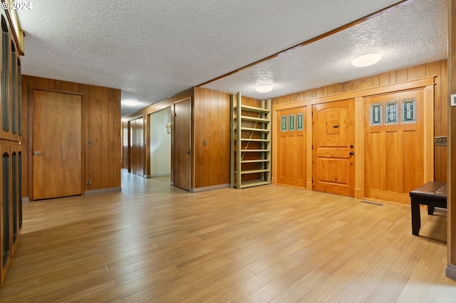 unfurnished living room with a textured ceiling, wood walls, and light hardwood / wood-style floors