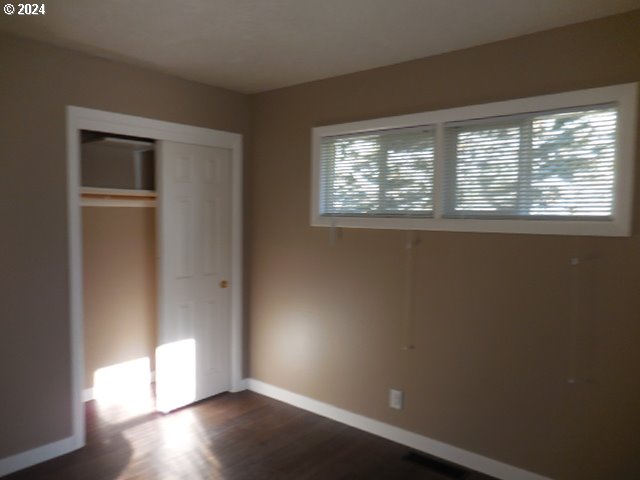 unfurnished bedroom with multiple windows, dark hardwood / wood-style flooring, and a closet