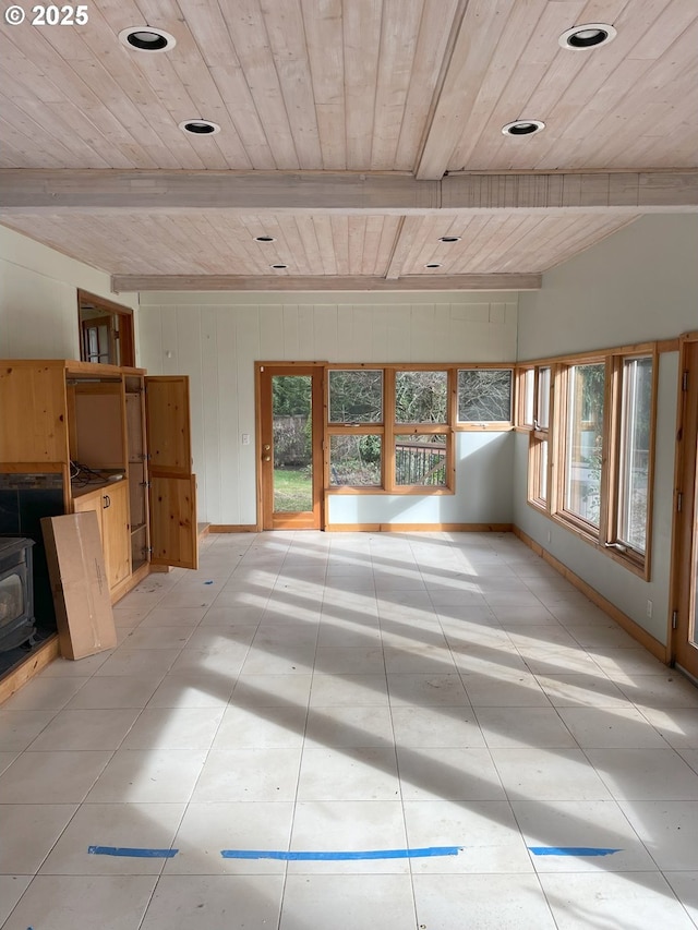 unfurnished living room featuring a wood stove, wood ceiling, baseboards, and beam ceiling