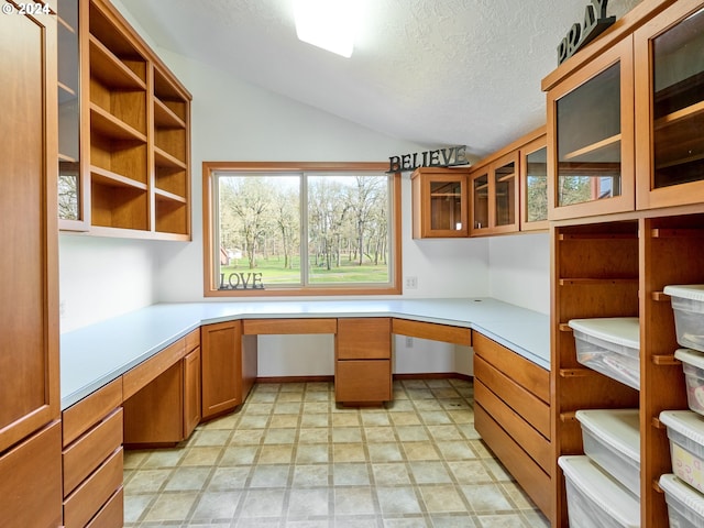 unfurnished office with built in desk, vaulted ceiling, light tile floors, and a textured ceiling