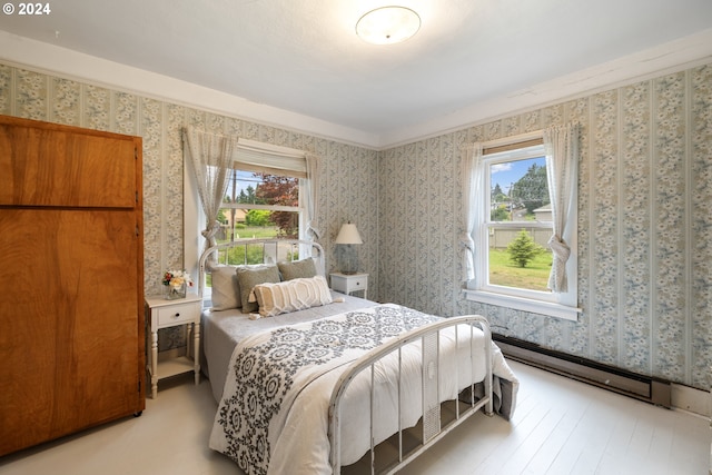 bedroom with multiple windows, crown molding, light wood-type flooring, and a baseboard heating unit