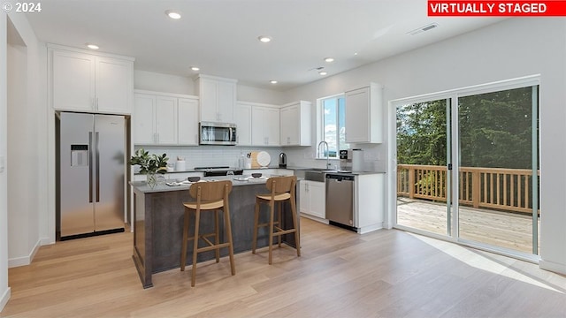 kitchen with a breakfast bar area, stainless steel appliances, a center island, light wood-type flooring, and white cabinets