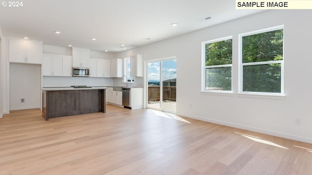 kitchen with white cabinets, backsplash, appliances with stainless steel finishes, light hardwood / wood-style flooring, and a center island