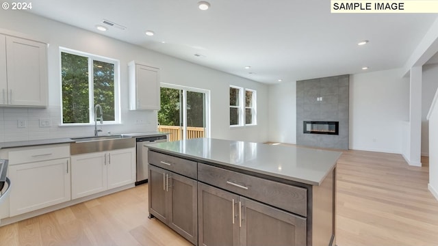 kitchen with a kitchen island, light hardwood / wood-style flooring, sink, stainless steel dishwasher, and white cabinets