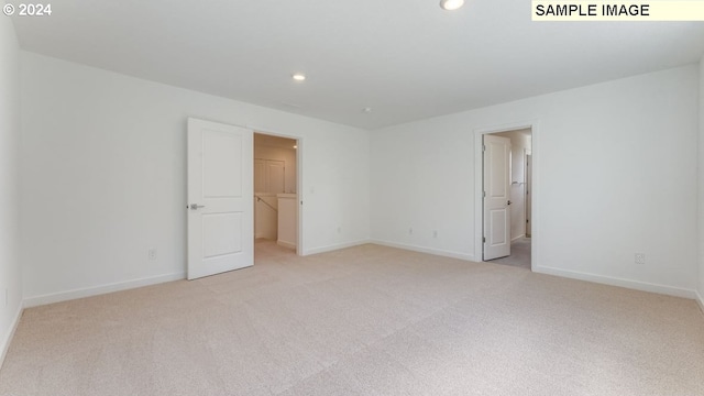 unfurnished bedroom featuring a spacious closet, ensuite bathroom, a closet, and light colored carpet