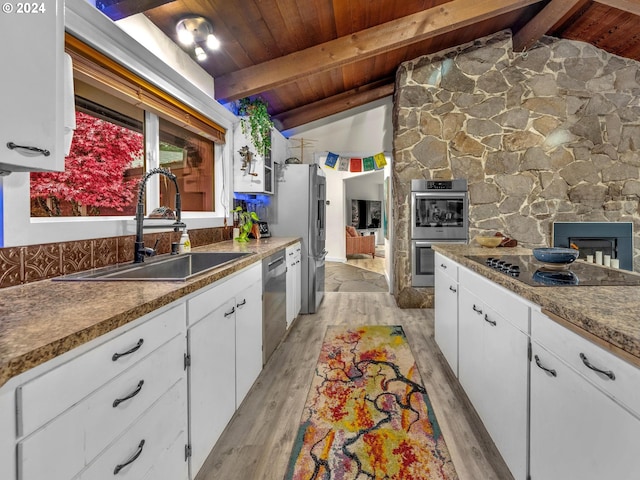 kitchen with appliances with stainless steel finishes, sink, vaulted ceiling with beams, and white cabinets