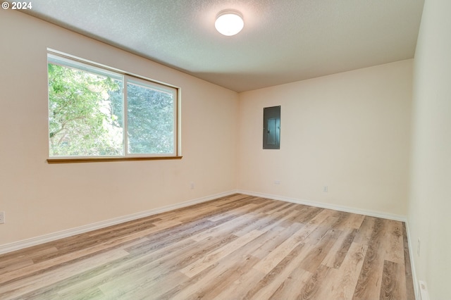 unfurnished room featuring light hardwood / wood-style floors, electric panel, and a textured ceiling