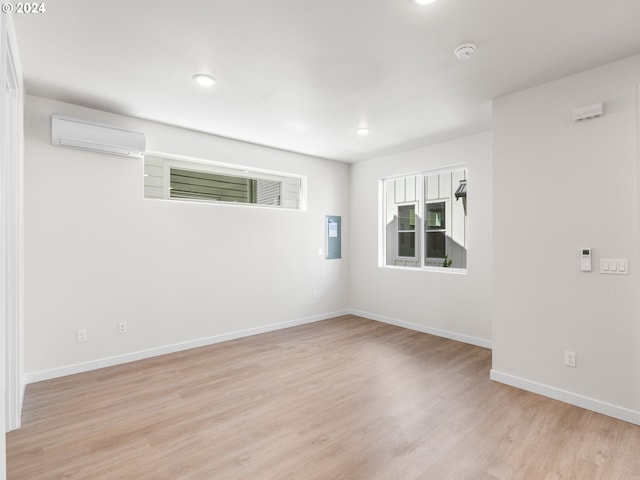 unfurnished room with electric panel, light hardwood / wood-style flooring, and a wall mounted AC