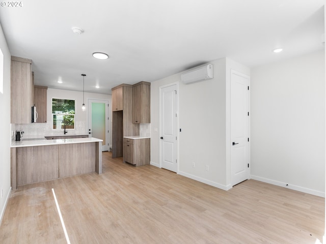 kitchen with an AC wall unit, hanging light fixtures, decorative backsplash, light wood-type flooring, and kitchen peninsula