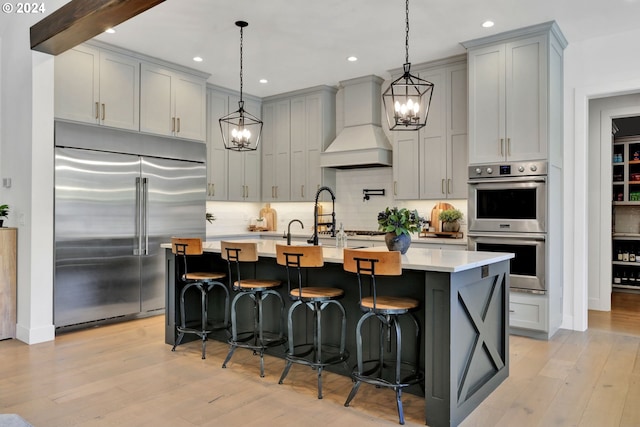 kitchen with custom range hood, stainless steel appliances, a center island with sink, and gray cabinetry