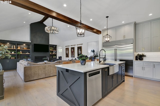 kitchen with a large fireplace, stainless steel appliances, light hardwood / wood-style flooring, pendant lighting, and a center island with sink