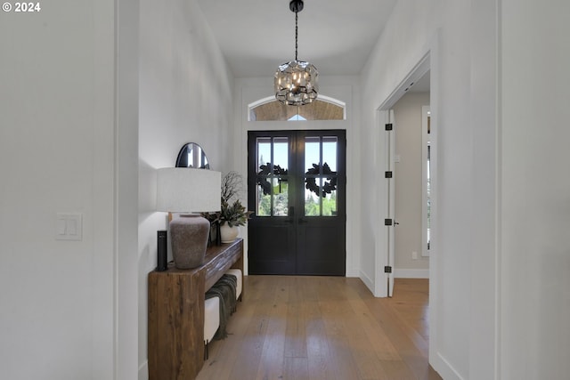 foyer entrance with an inviting chandelier, light hardwood / wood-style flooring, and french doors