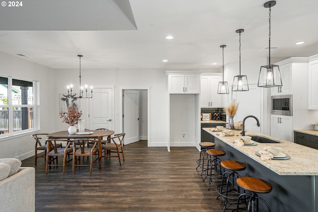 kitchen with hanging light fixtures, sink, white cabinets, and light stone countertops