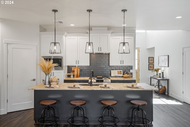 kitchen with a center island with sink, white cabinets, and light stone countertops