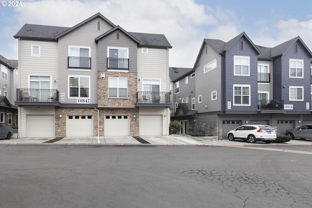 multi unit property featuring a garage, stone siding, driveway, and roof with shingles