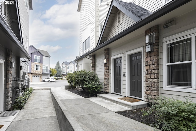 entrance to property featuring a residential view, stone siding, and roof with shingles