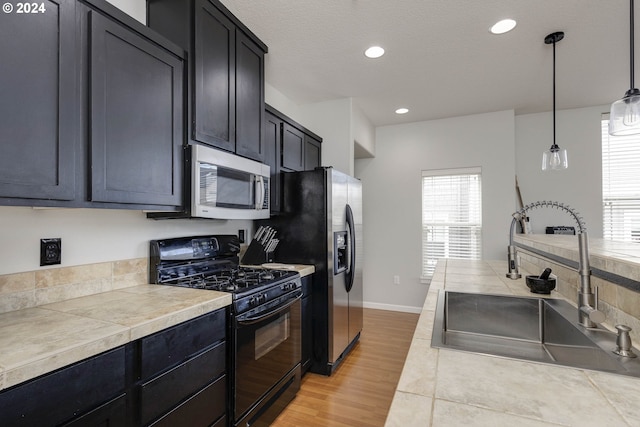 kitchen featuring black gas stove, a sink, light countertops, stainless steel microwave, and dark cabinets