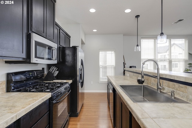 kitchen featuring light wood-type flooring, stainless steel appliances, sink, pendant lighting, and tile counters