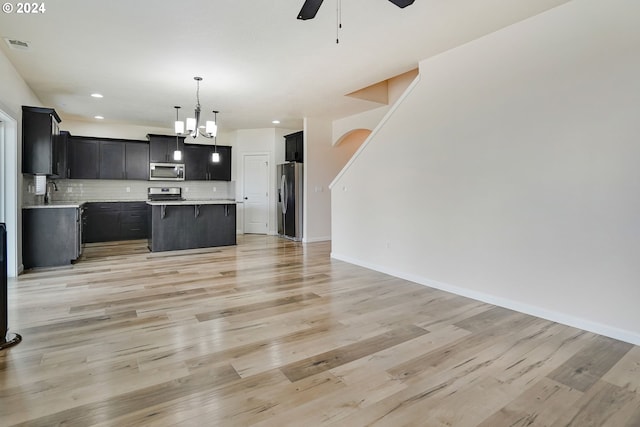 kitchen with tasteful backsplash, a kitchen island, light hardwood / wood-style flooring, appliances with stainless steel finishes, and ceiling fan with notable chandelier