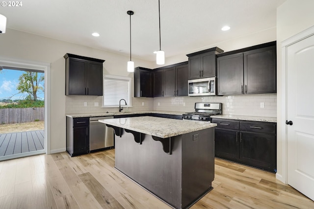 kitchen with pendant lighting, tasteful backsplash, a kitchen island, light hardwood / wood-style flooring, and appliances with stainless steel finishes