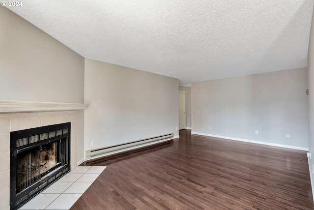 unfurnished living room featuring baseboard heating, a textured ceiling, a tiled fireplace, and light wood-type flooring